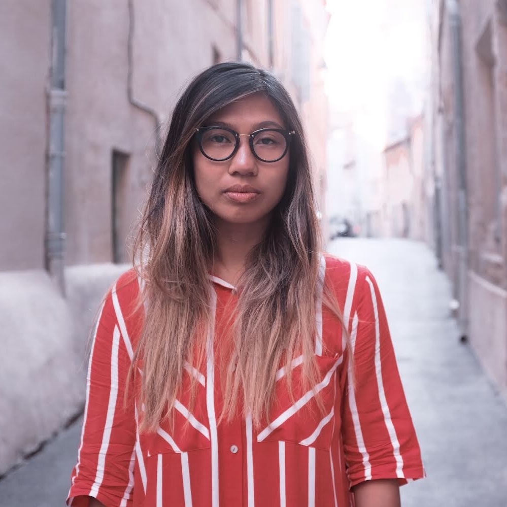 Kristel standing in a narrow stone street wearing a red and white striped shirt. 